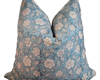 May include: A square throw pillow featuring a blue fabric base with a repeating off-white floral pattern. The design consists of detailed blossoms and leafy vines covering the entire surface, creating a dense botanical motif across the pillow.