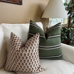 May include: Two decorative throw pillows on a white couch. One pillow has a black and white floral pattern on a beige background. The other pillow is green with black stripes.