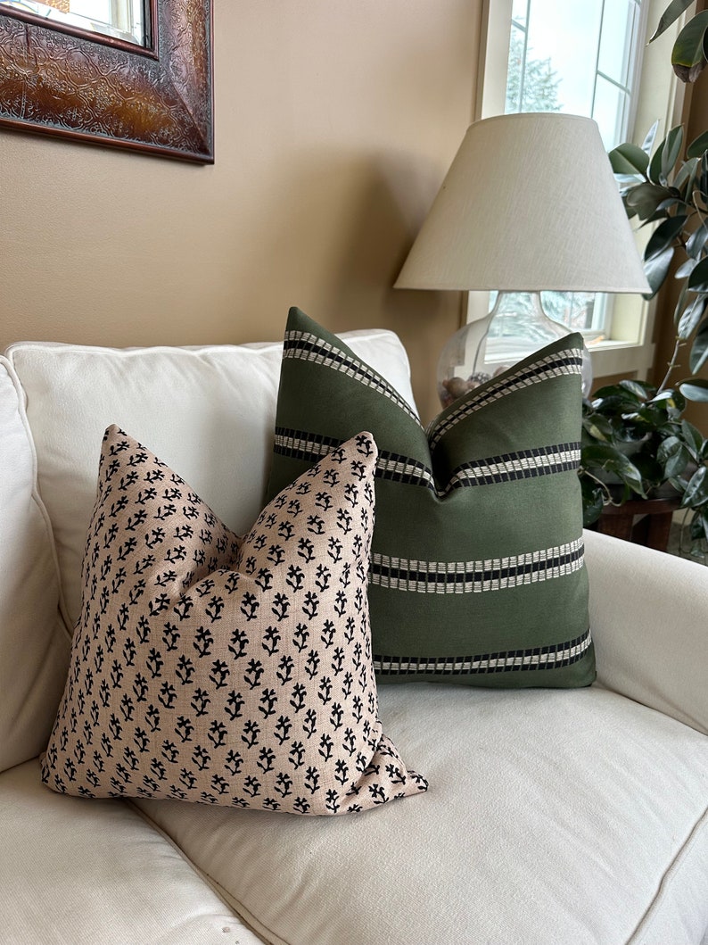 May include: Two decorative throw pillows on a white couch. One pillow has a black and white floral pattern on a beige background. The other pillow is green with black stripes.