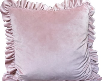 May include: A square throw pillow in a soft, dusty pink velvet fabric. The pillow features a gathered ruffle trim along all four edges, creating a decorative border. The surface of the pillow has a smooth, uniform texture with a subtle sheen.