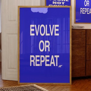 Könnte beinhalten: Drei gerahmte Poster mit motivierenden Zitaten. Das größte Poster zeigt "EVOLVE OR REPEAT" in weißem Text auf blauem Hintergrund. Zwei kleinere Poster zeigen "DON'T LOOK BACK YOURE NOT GOING" und "EVOLVE OR REPEAT". Alle sind in Holzrahmen.
