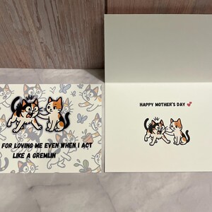 May include: A greeting card with a cat illustration. The card says "Happy Mother's Day" and features two cats with the text "Thanks for loving me even when I act like a gremlin".