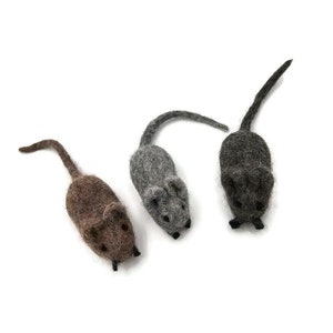 May include: Three felt mice toys in different colors: gray, brown, and dark gray. The mice are all lying on a white surface.