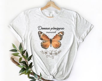May include: A white t-shirt with a brown and orange monarch butterfly graphic and the text "Danaus plexippus monarch" printed on the front.