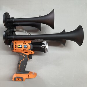 May include: A black and orange power tool with two black air horns attached. The tool has a black trigger and a black handle. The air horns are attached to the tool with a silver connector.