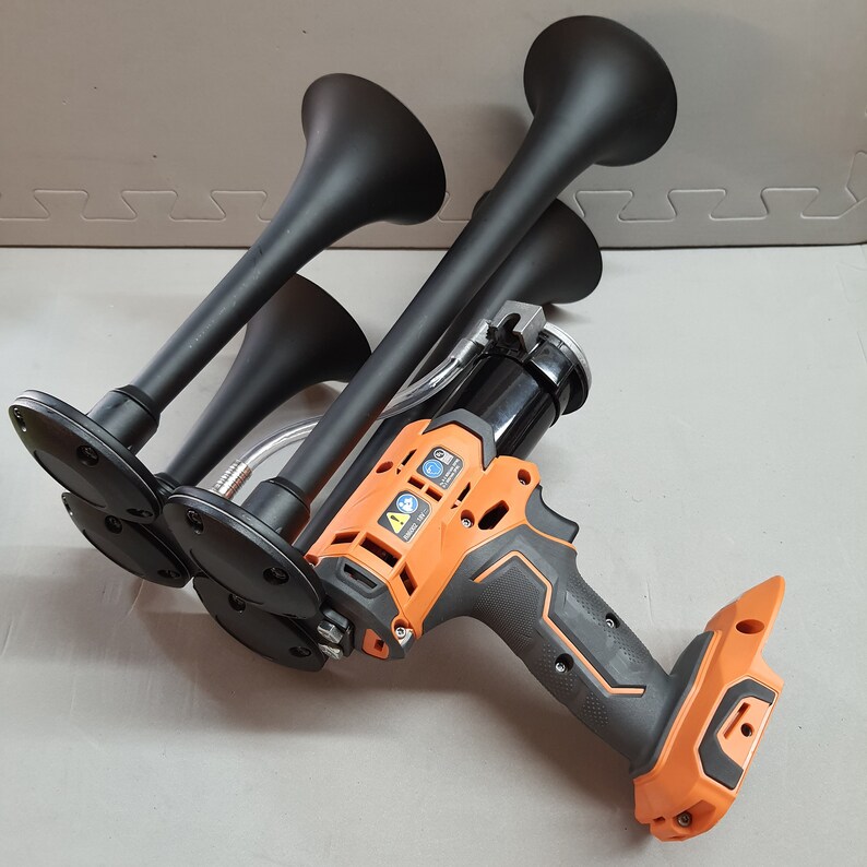 May include: A black air horn with a black and orange electric air compressor. The air horn has four separate horns connected together.
