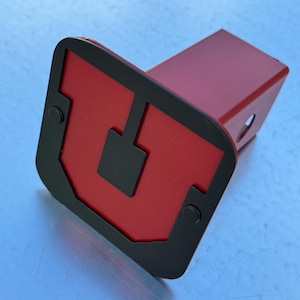 May include: A red and black metal hitch cover with a black outline and a red "U" in the center.