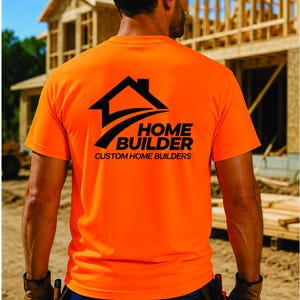 May include: A bright neon orange short-sleeved t-shirt featuring a black graphic on the back. The graphic displays a house silhouette above the text HOME BUILDER and CUSTOM HOME BUILDERS in a bold, sans-serif font, centered on the shirt back.