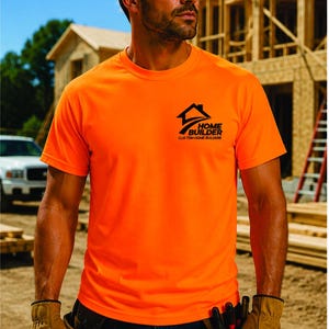 May include: A bright neon orange short-sleeved t-shirt featuring a black graphic logo on the left chest that reads Home Builder Custom Home Builders with a house icon. The shirt is worn with dark blue jeans and a brown leather tool belt.