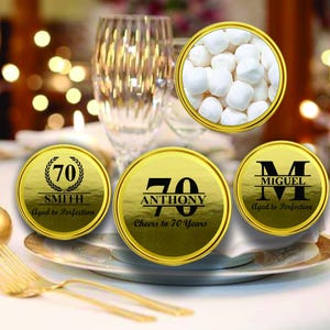 May include: Gold favor boxes with personalized labels for a 70th birthday celebration. The labels feature the names "Smith", "Anthony", and "Miguel" with the number 70 and the phrase "Aged to Perfection".