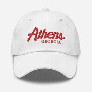 Op de afbeelding: Witte baseballpet met rode geborduurde tekst die "Athens Georgia" zegt.