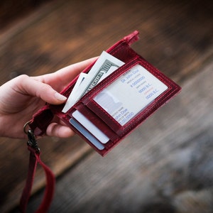 May include: A red leather wallet with a lanyard, holding a dollar bill, credit cards, and a business card with the text "Dr. John Doe" and "0000 B.C."