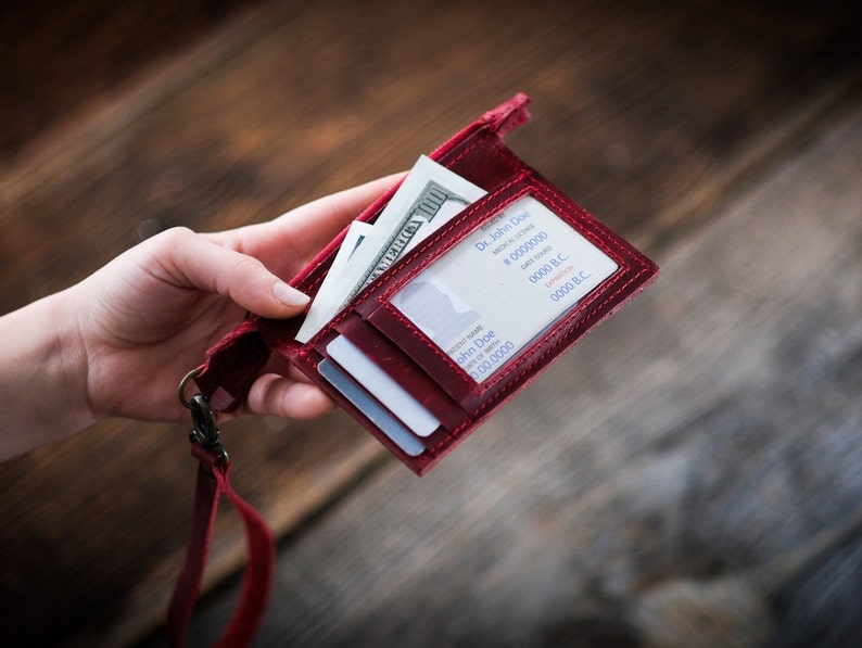 May include: A red leather wallet with a lanyard, holding a dollar bill, credit cards, and a business card with the text "Dr. John Doe" and "0000 B.C."