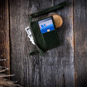 May include: A dark green leather wallet with a zipper closure and a strap. The wallet is open and contains several credit cards.