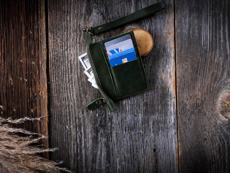 May include: A dark green leather wallet with a zipper closure and a strap. The wallet is open and contains several credit cards.