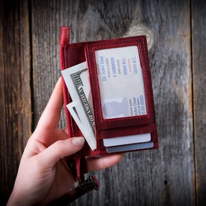 May include: A red leather wallet with a clear plastic window displaying a medical license with the name "Dr. John Doe" and license number "# 0000000". The wallet also contains cash and credit cards.