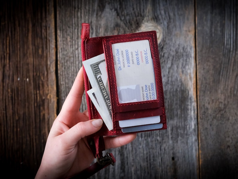 May include: A red leather wallet with a clear plastic window displaying a medical license with the name "Dr. John Doe" and license number "# 0000000". The wallet also contains cash and credit cards.