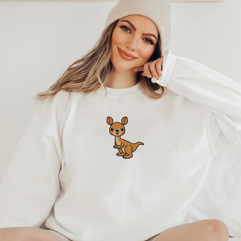 May include: White sweatshirt with a cartoon kangaroo graphic. The kangaroo is brown with a light brown belly and a pink nose.