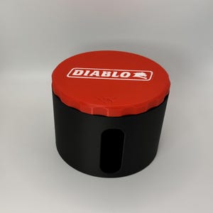 May include: A black cylindrical container with a red lid. The lid features the word "DIABLO" in white within a white rectangular border. The container has a rectangular opening on the side.