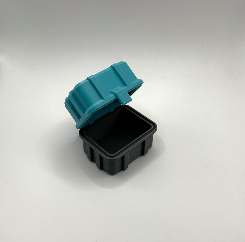 Pu&ograve; includere: Una scatola di contenimento in plastica turchese con un coperchio nero. Il coperchio &egrave; aperto e la scatola &egrave; vuota.
