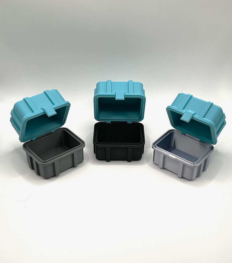 Pu&ograve; includere: Tre piccole scatole di immagazzinaggio in plastica aperte. Le scatole sono di colore turchese, nero e grigio.