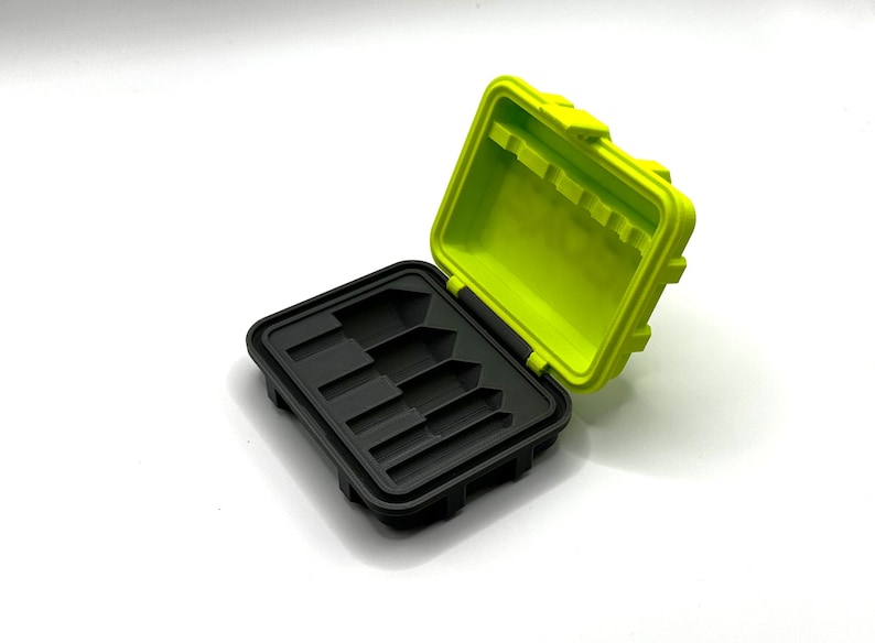 Pode incluir: Uma pequena caixa de armazenamento preta e verde com uma tampa aberta. A caixa tem seis compartimentos para guardar pequenos objetos.