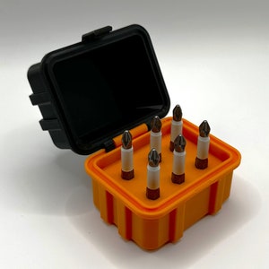 Op de afbeelding: Een set van zes schroevendraaierbits in een zwarte en oranje draagkoffer. De bits zijn in een rasterpatroon gerangschikt en zijn allemaal even groot.