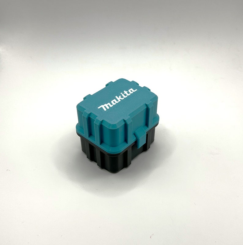 Pu&ograve; includere: Una cassetta degli attrezzi in plastica blu turchese con la scritta "Makita" stampata in bianco sulla parte superiore. La cassetta ha una base nera.