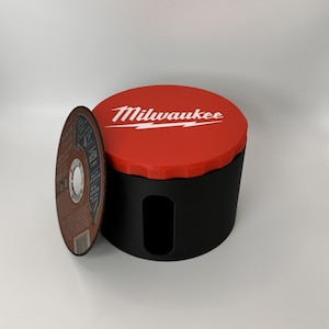 May include: A black and red Milwaukee tool storage container with a red lid and the Milwaukee logo in white. A 4 1/2 inch grinding disc is leaning against the container.