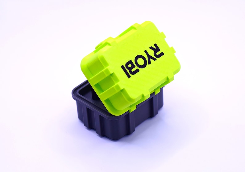 K&ouml;nnte beinhalten: Eine schwarze und neongr&uuml;ne Aufbewahrungsbox. Der Deckel, neongr&uuml;n, tr&auml;gt den schwarzen Aufdruck "RYOBI". Der Boden der Box ist schwarz. Die Box hat eine Reihe von Rillen.