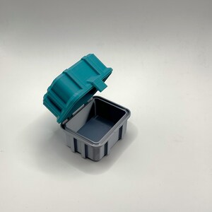 Pu&ograve; includere: Una scatola di plastica turchese con un interno grigio. Il coperchio &egrave; aperto e la scatola &egrave; vuota.