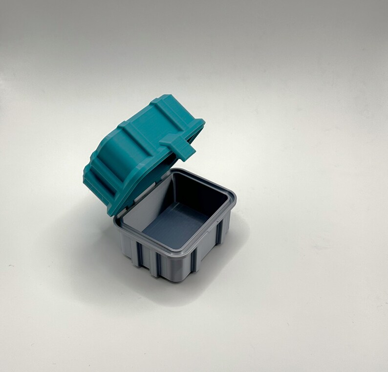 Pu&ograve; includere: Una scatola di plastica turchese con un interno grigio. Il coperchio &egrave; aperto e la scatola &egrave; vuota.