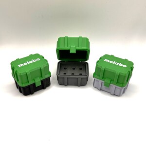 May include: Three small green and gray plastic tool boxes with the word "metabo" printed on the side. The boxes are open and have a gray interior with small compartments.