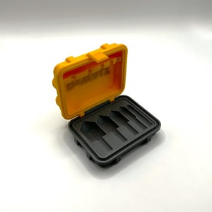 May include: A yellow plastic case with a black interior. The case has five slots for holding small items. The case is open and the slots are visible.