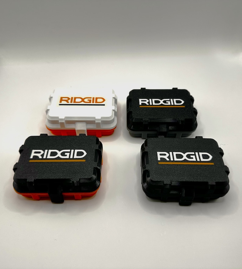 May include: Four small black and white plastic boxes with the word "RIDGID" printed on the top. The boxes are arranged in a square pattern.