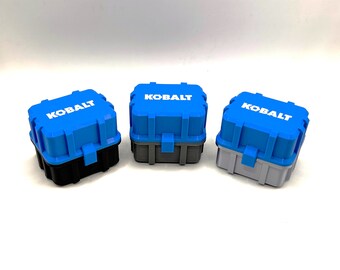 Op de afbeelding: Drie kleine blauwe plastic opbergdozen met het woord "KOBALT" in wit op de voorkant. De dozen zijn in drie verschillende kleuren: zwart, grijs en lichtgrijs.
