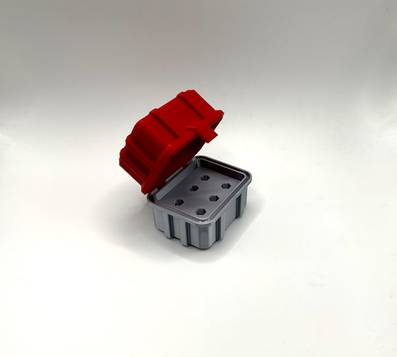 Op de afbeelding: Een rode en grijze plastic opbergdoos met een scharnierend deksel en meerdere compartimenten. Het deksel is open en de doos is leeg.