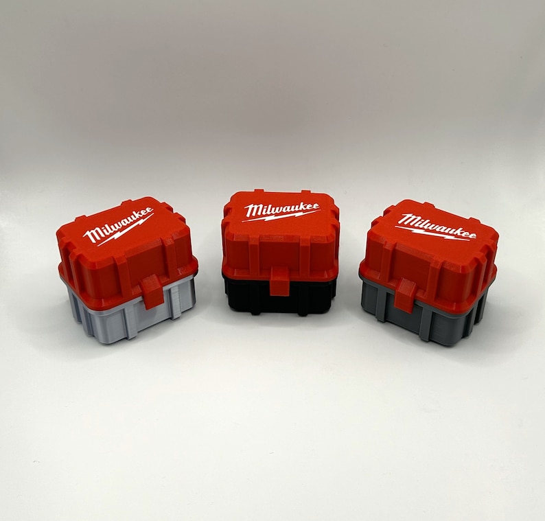 Op de afbeelding: Drie rode en grijze plastic gereedschapskisten met het woord "Milwaukee" in wit gedrukt op de bovenkant van elke doos.