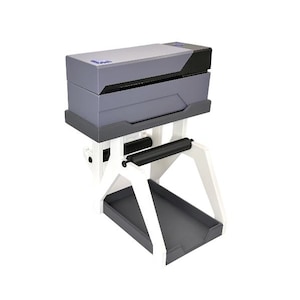 May include: A gray and black industrial machine with a white support structure. The machine has a rectangular shape with a tray at the bottom and a roller in the middle. The machine is designed for industrial use.