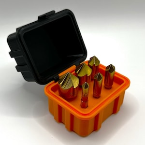 Op de afbeelding: Een set van zes goudkleurige boortjes in een feloranje plastic koffer met een zwart deksel. De koffer heeft een geribbeld ontwerp.