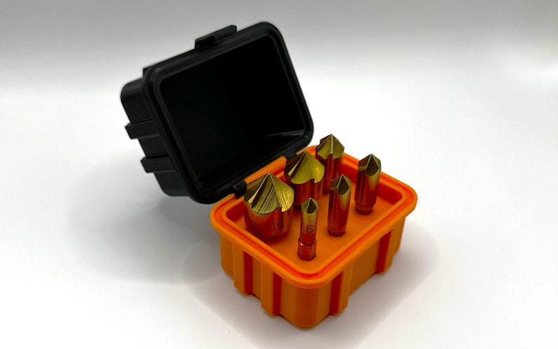 Op de afbeelding: Een set van zes goudkleurige boortjes in een feloranje plastic koffer met een zwart deksel. De koffer heeft een geribbeld ontwerp.