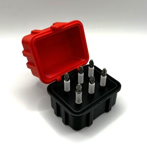 Op de afbeelding: Een rode en zwarte plastic koffer met een set van acht schroevendraaierbits. De bits zijn gerangschikt in een rasterpatroon in de koffer.