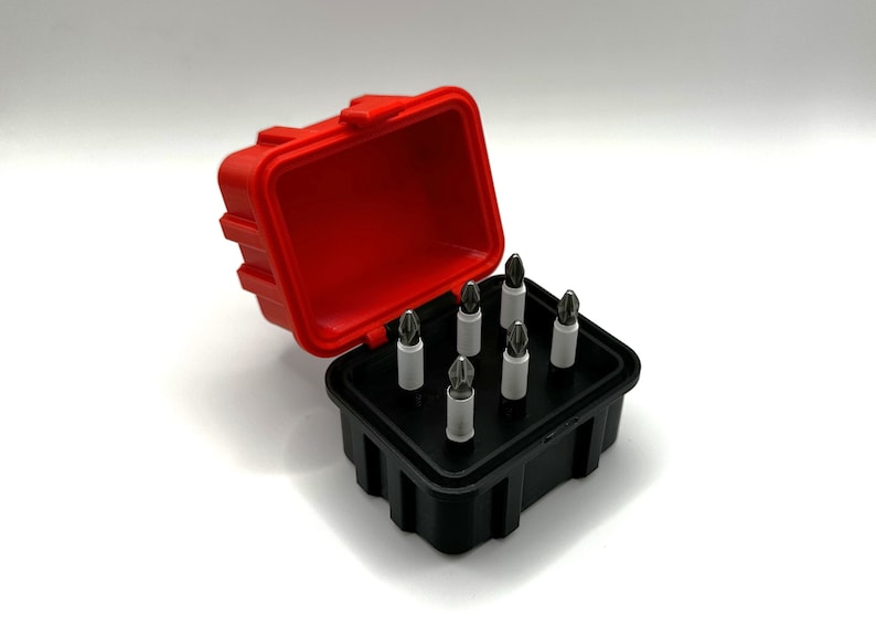 Op de afbeelding: Een rode en zwarte plastic koffer met een set van acht schroevendraaierbits. De bits zijn gerangschikt in een rasterpatroon in de koffer.