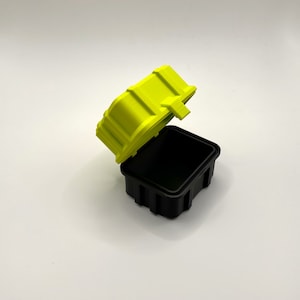 K&ouml;nnte beinhalten: Eine kleine, rechteckige schwarze Box mit einem leuchtend gelben Deckel. Der Deckel ist ge&ouml;ffnet und die Box ist leer.