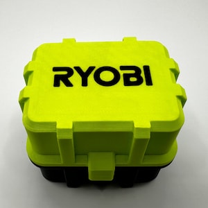 K&ouml;nnte beinhalten: Ein limettengr&uuml;ner und schwarzer Aufbewahrungsbeh&auml;lter mit dem Wort "RYOBI" in schwarzen Blockbuchstaben auf der Oberseite. Der Beh&auml;lter hat eine rechteckige Form mit einer strukturierten Oberfl&auml;che, wahrscheinlich f&uuml;r Werkzeuge oder Ger&auml;te.