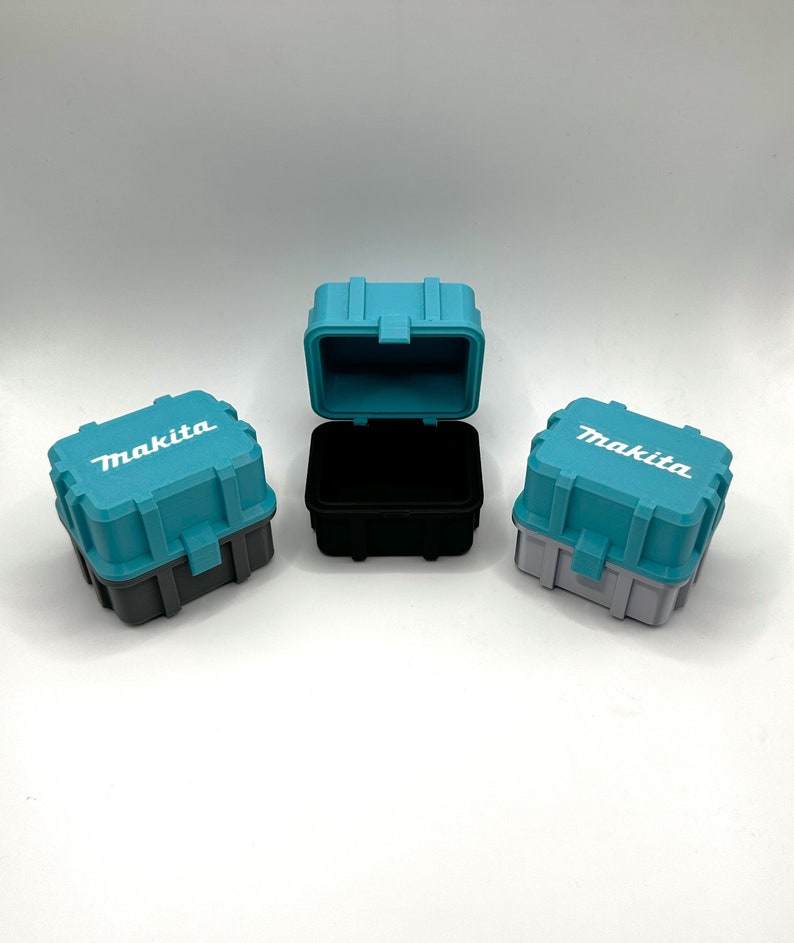 Pu&ograve; includere: Tre piccole scatole di immagazzinaggio in plastica blu turchese con coperchi neri e grigi. Le scatole hanno la scritta "Makita" stampata in bianco sul davanti.