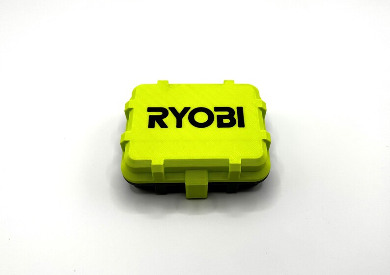 Pode incluir: Uma pequena caixa de armazenamento de pl&aacute;stico amarelo brilhante com a palavra "RYOBI" impressa em letras pretas na parte superior.