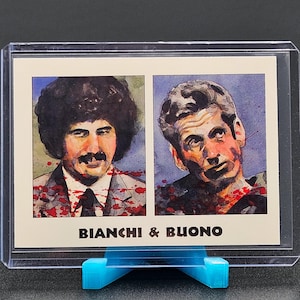 May include: A trading card featuring two portraits with the text "BIANCHI & BUONO". The portraits are of two men, one with a large afro and mustache, the other with short hair. The card is in a clear plastic sleeve and displayed on a blue stand.
