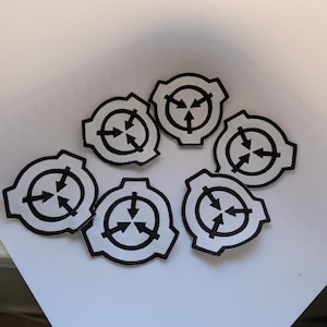 May include: Six white patches with a black border and a black arrow design. The patches are arranged on a white surface. The design features a circle with three arrows pointing inward.