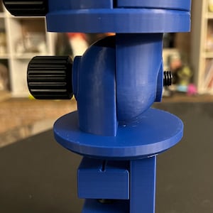 May include: A blue plastic camera tripod with adjustable legs and a ball head. The tripod has a hexagonal base and two knobs for adjusting the angle of the head.